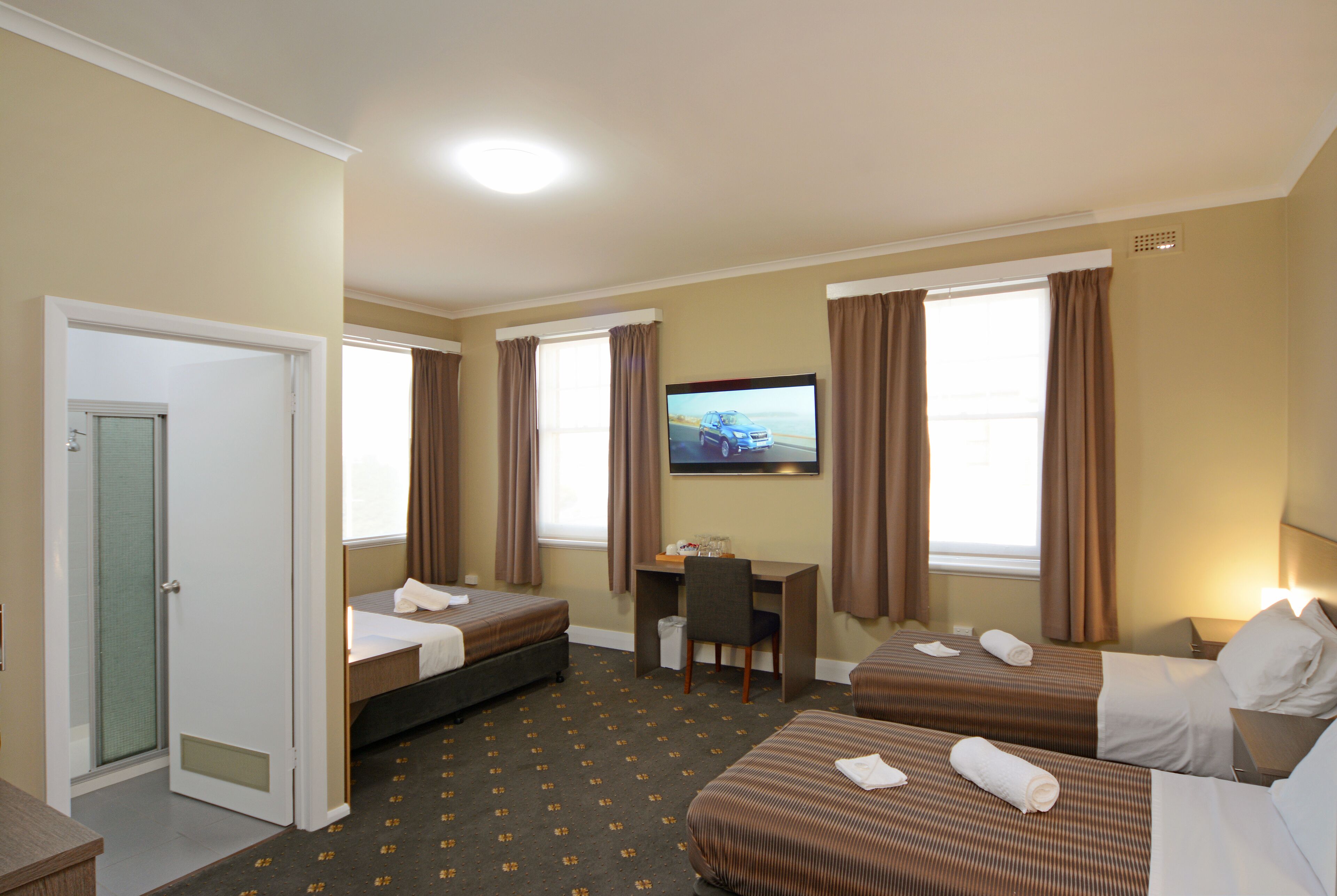 A hotel room with two beds, a desk, a TV, and a shower.