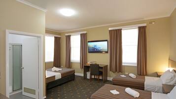 A hotel room with two beds, a desk, a TV, and a shower.