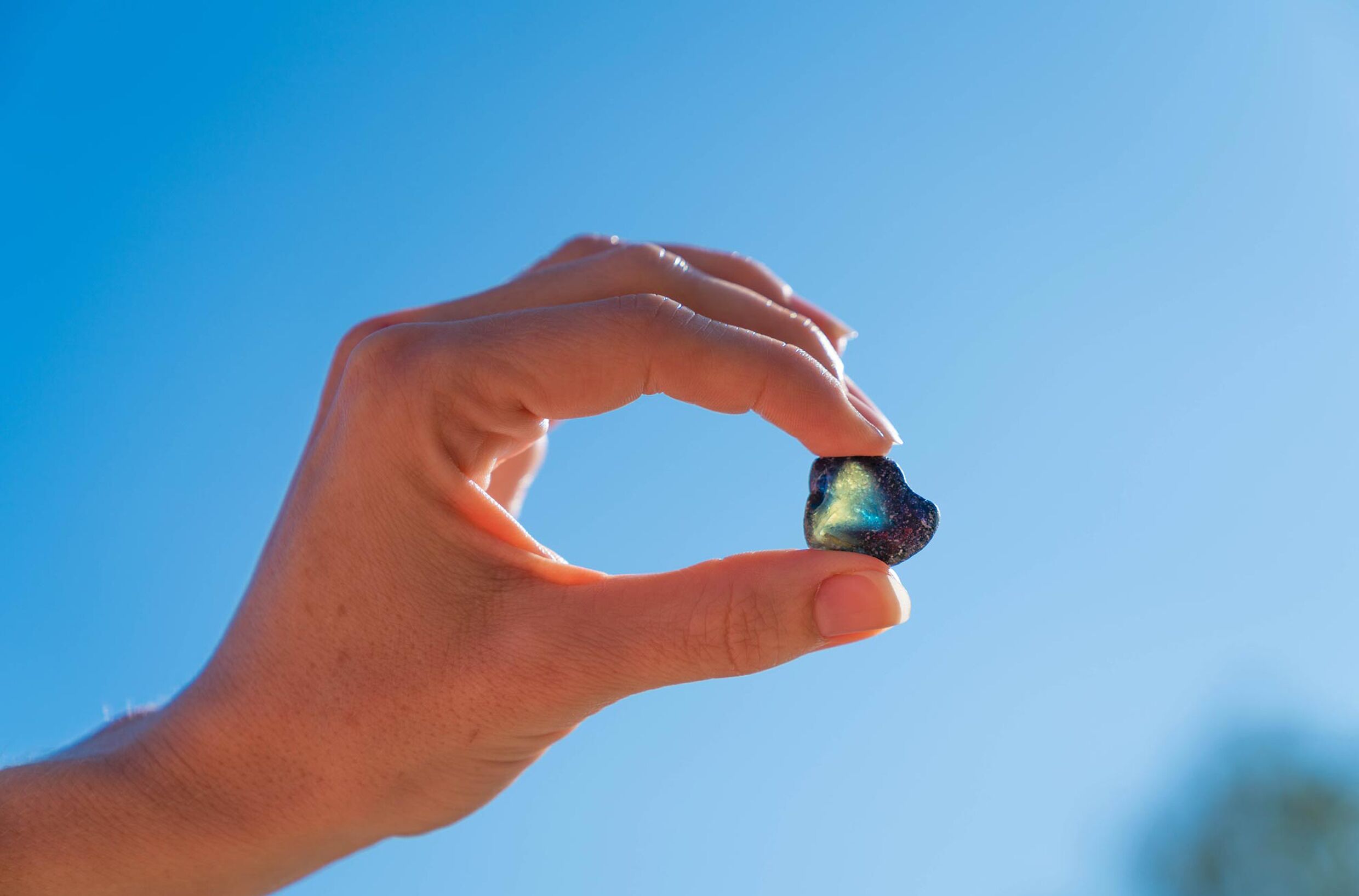 A hand holding a small, iridescent object against a clear blue sky.