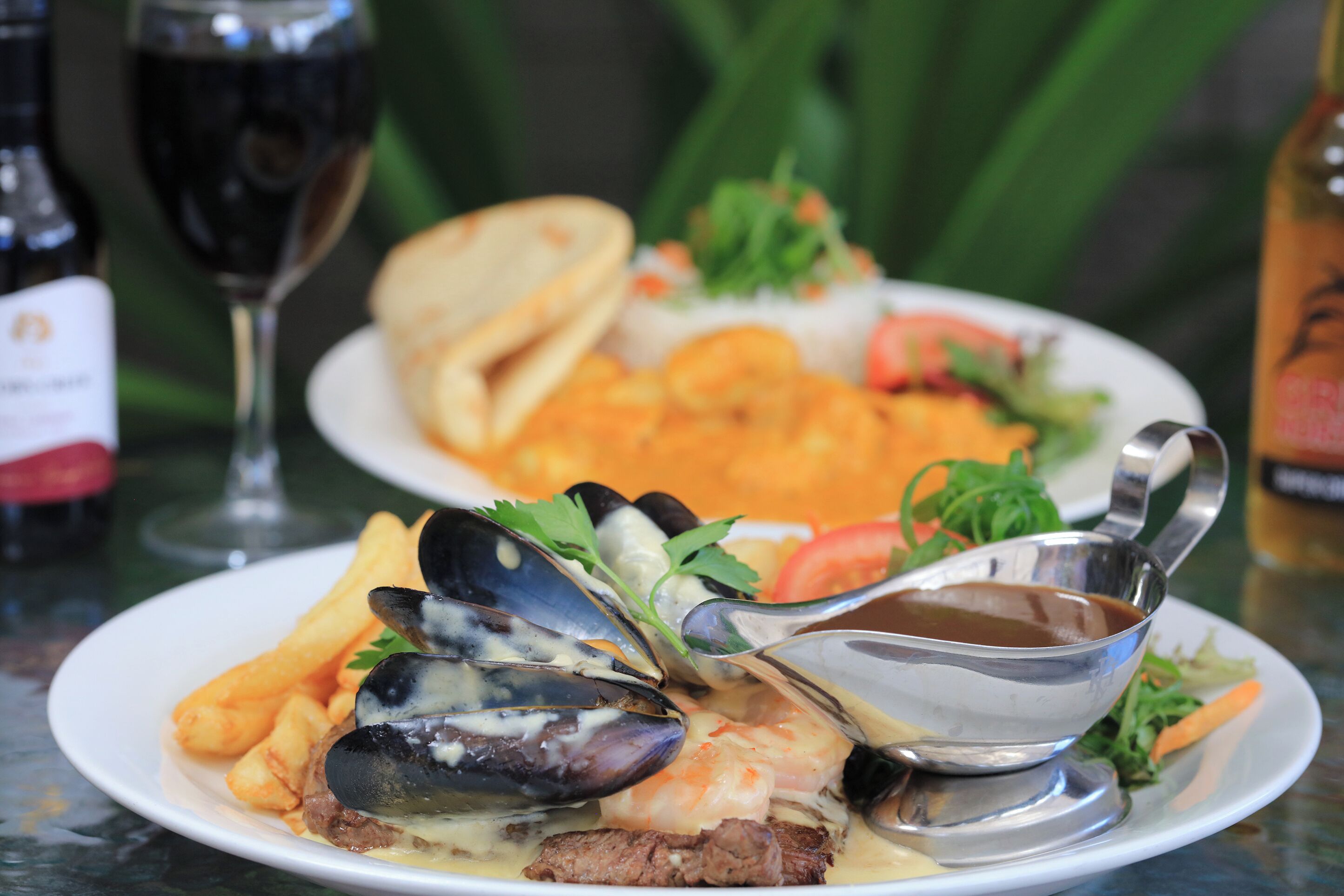 A seafood dish with mussels, shrimp, and steak, accompanied by fries and a glass of red wine.