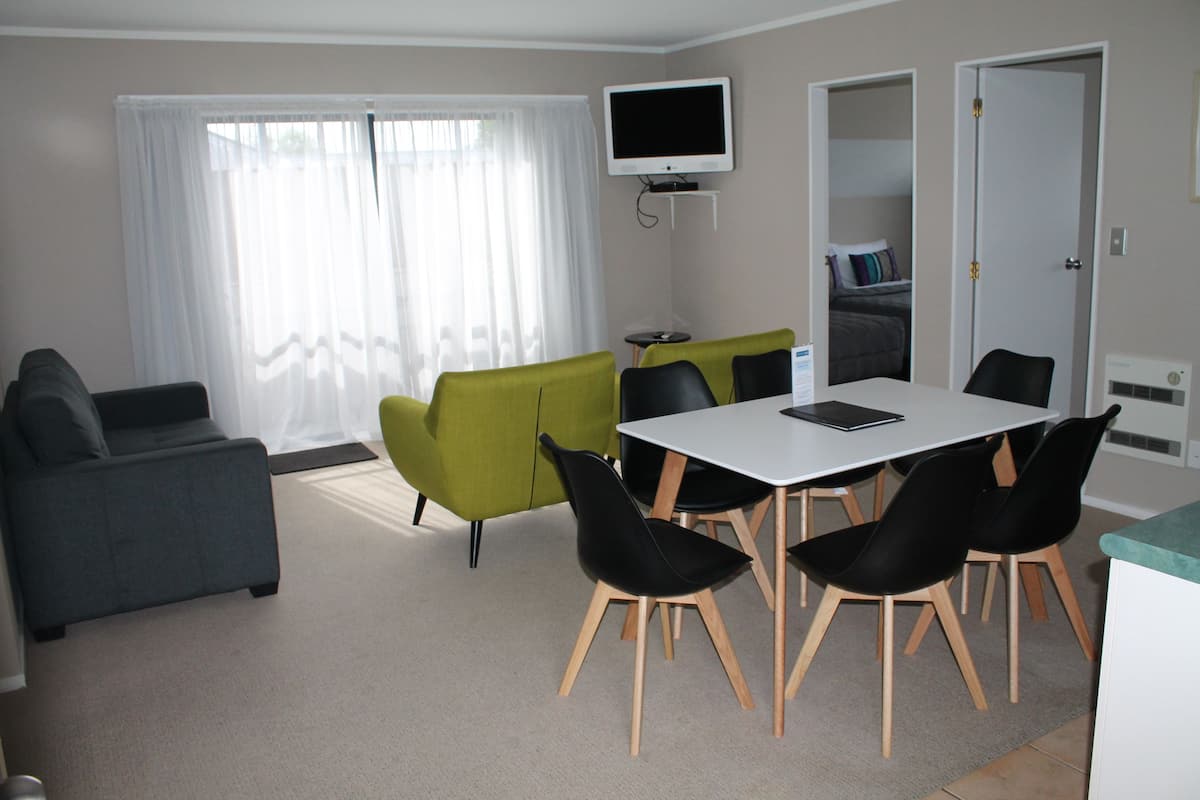 A modern living room with a dining table, chairs, a sofa, and a TV mounted on the wall.