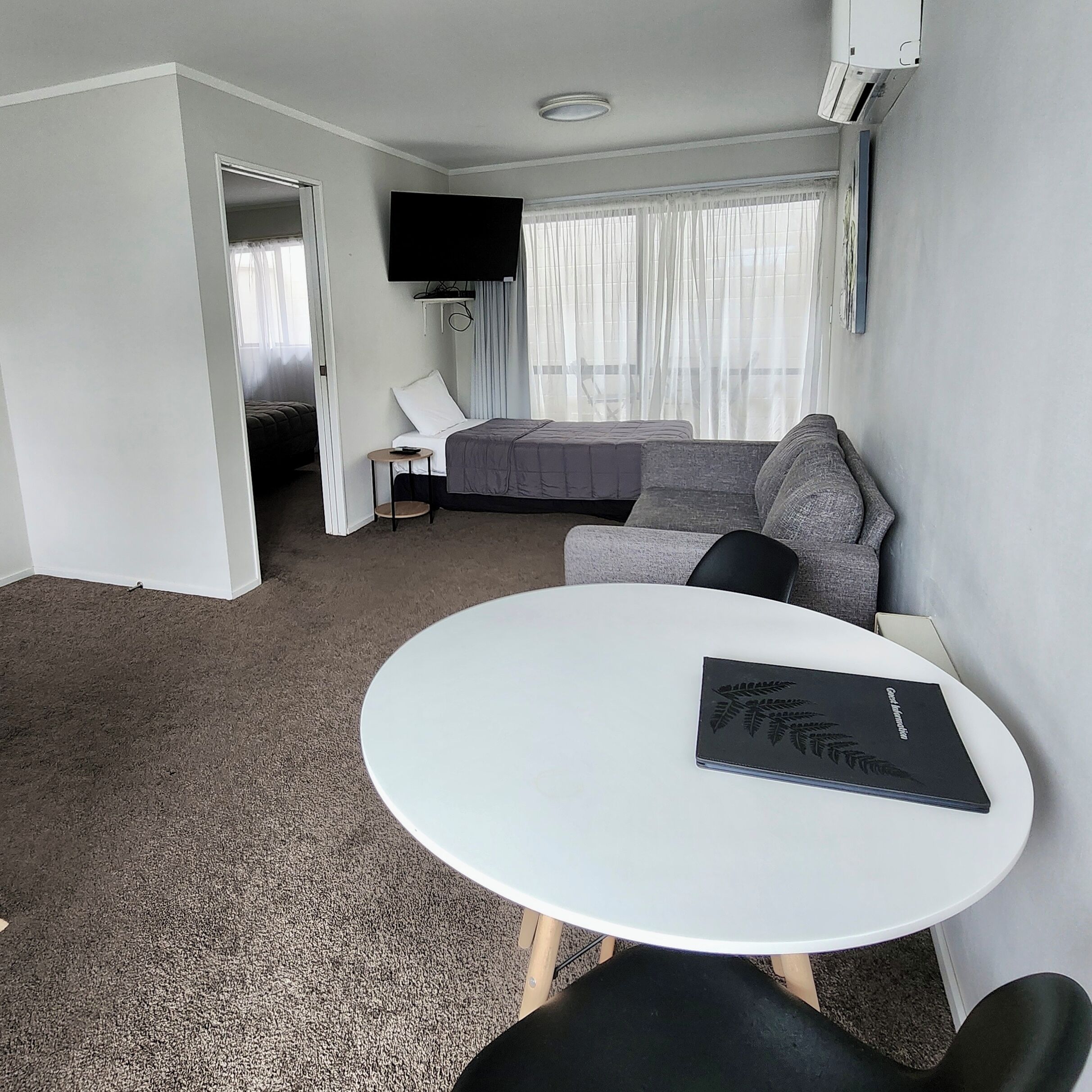A hotel room with a bed, a sofa, a small table, and a TV mounted on the wall.