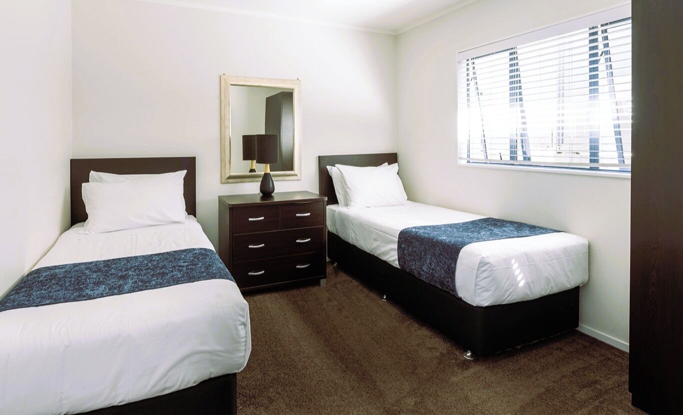 A hotel room with two beds, a dresser, a mirror, and a window with blinds.