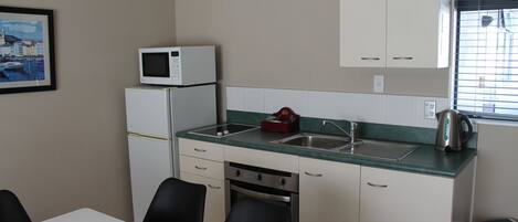 Ett kompakt kök med mikrovågsugn, diskho och vattenkokare. Det finns ett matbord med stolar och en inramad tavla på väggen.