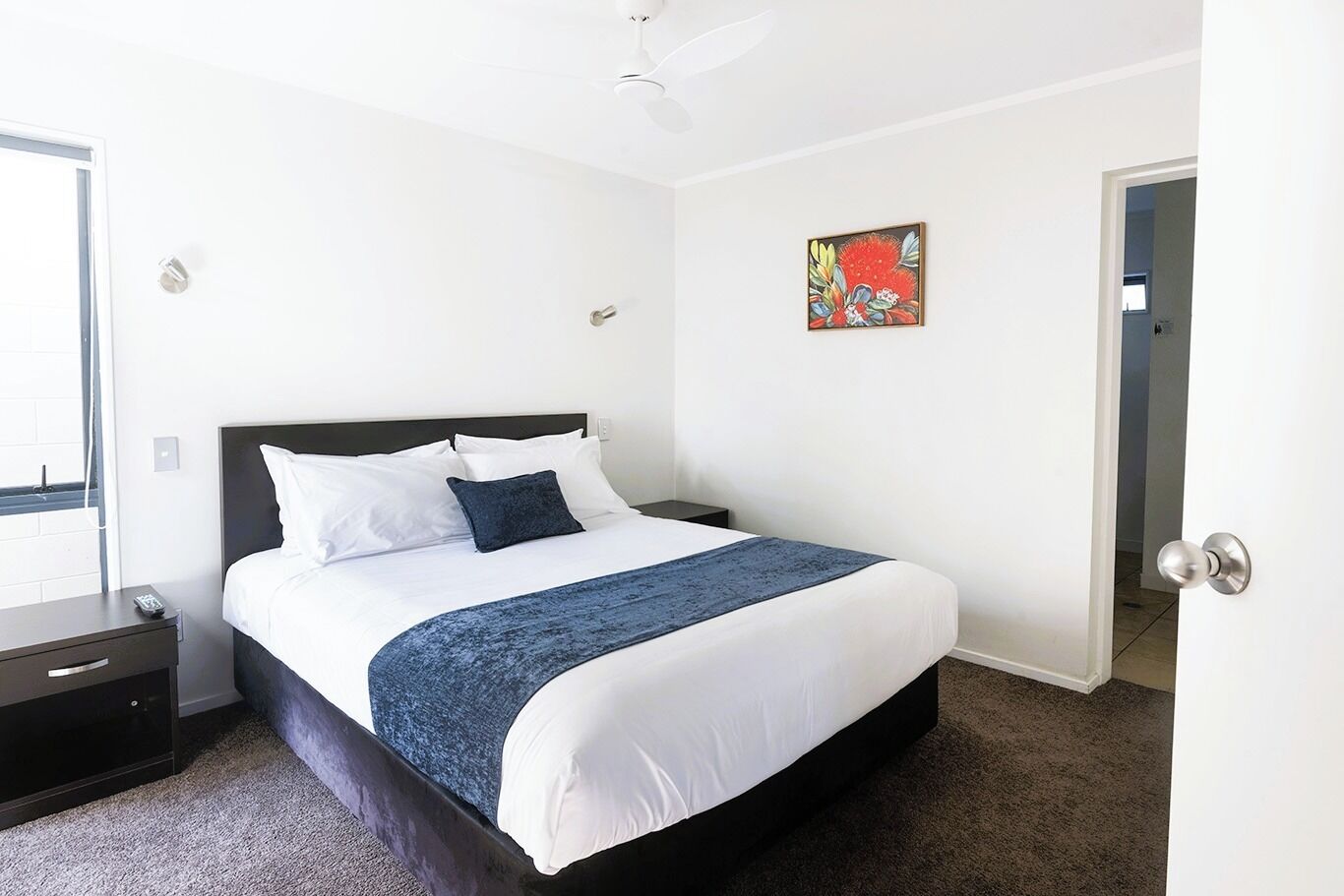 A hotel room with a bed, a nightstand, a door, and a ceiling fan.
