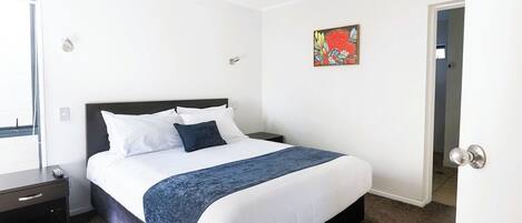 A hotel room with a bed, a nightstand, a door, and a ceiling fan.