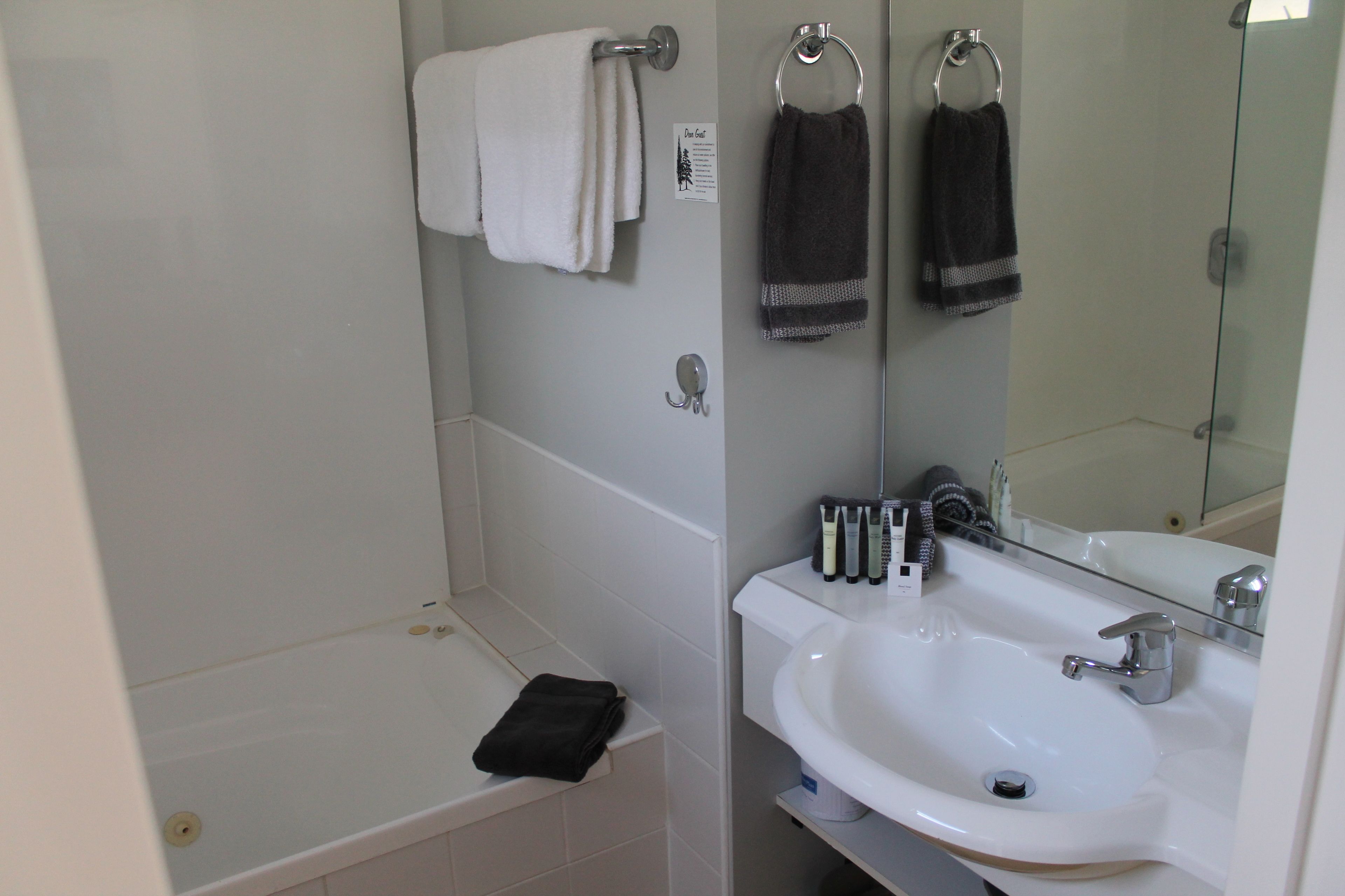 Un baño con una bañera blanca, un lavabo con espejo y dos toallas colgadas en ganchos.