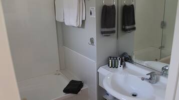 Une salle de bain avec une baignoire blanche, un lavabo avec un miroir et deux serviettes suspendues à des crochets.