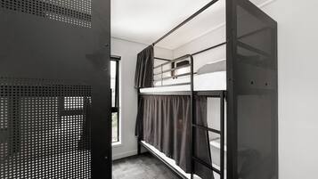A bunk bed room with a metal frame, a window with curtains, and a door with a metal mesh.