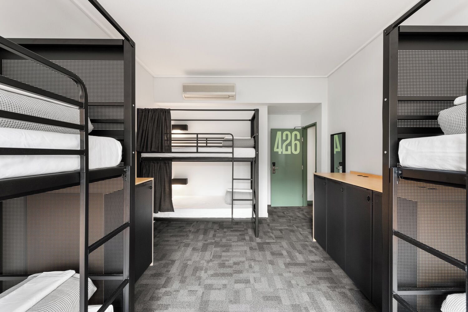 A dormitory room with bunk beds, a door labeled "426", a small desk, and a mirror.