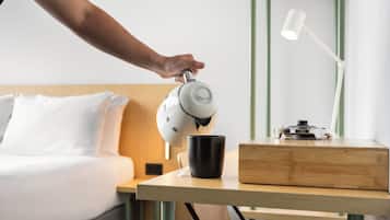 Een hand giet koffie uit een machine in een kopje op een houten tafel in een hotelkamer.