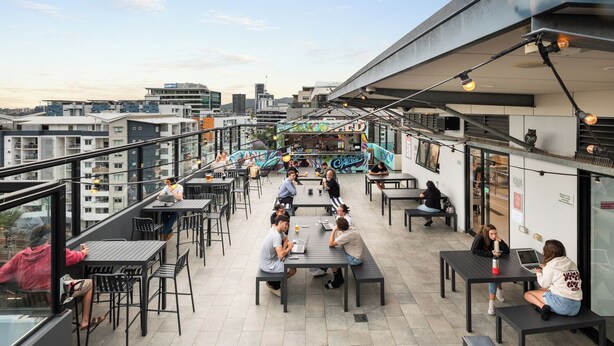 Une terrasse extérieure avec des tables et des chaises, un bar en arrière-plan et une vue sur la ville.