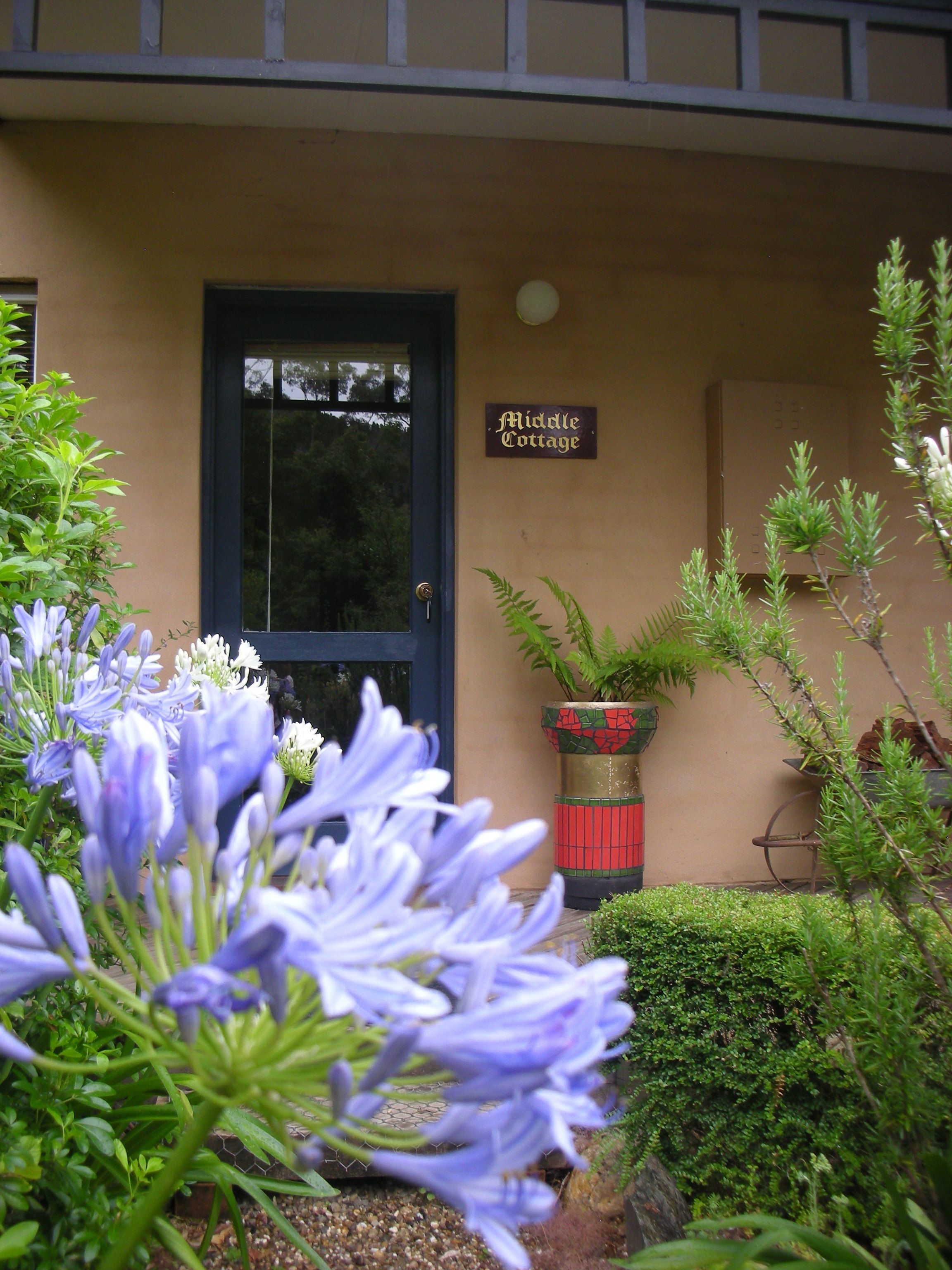 A building with a dark blue door, a sign reading "Middle Cottage," and a potted plant with green foliage.