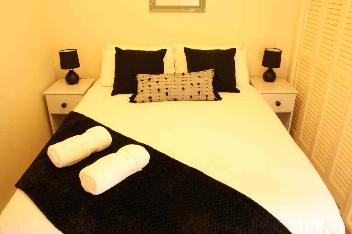 Una cama bien tendida con ropa de cama blanco y negro, dos lámparas de noche y una manta blanco y negro.