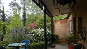 A wooden deck with a table and chairs, surrounded by lush greenery and flowering plants. - Merrimeet Cottages (Bright)