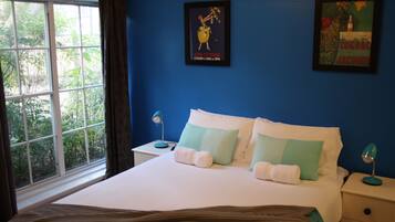 Ein Schlafzimmer mit einem großen Bett, zwei Nachttischen, einem Fenster mit Vorhängen und zwei an der Wand hängenden Bildern.