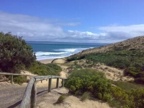 Un paisaje costero con una playa arenosa, un camino de madera y vistas al océano.