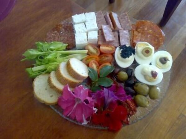 Una fuente de vidrio con diversos alimentos, como pan, queso, aceitunas y flores.