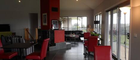 A modern living room with a dining area, featuring a fireplace, red and black furniture, and large windows with a view.