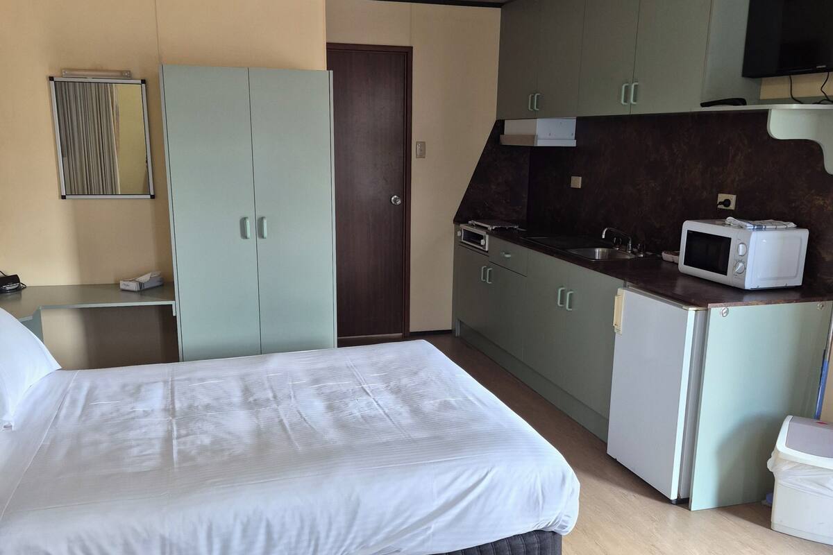 Habitación de hotel compacta con cama, kitchenette pequeña, escritorio y armario.