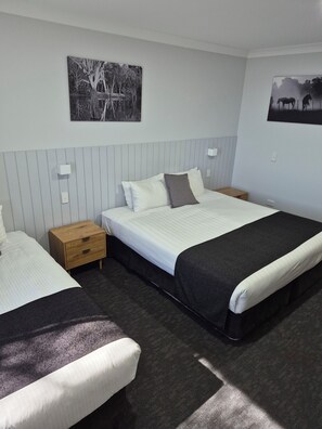 Une chambre d’hôtel avec deux lits, une table de chevet en bois, une lampe fixée au mur et deux tableaux encadrés.