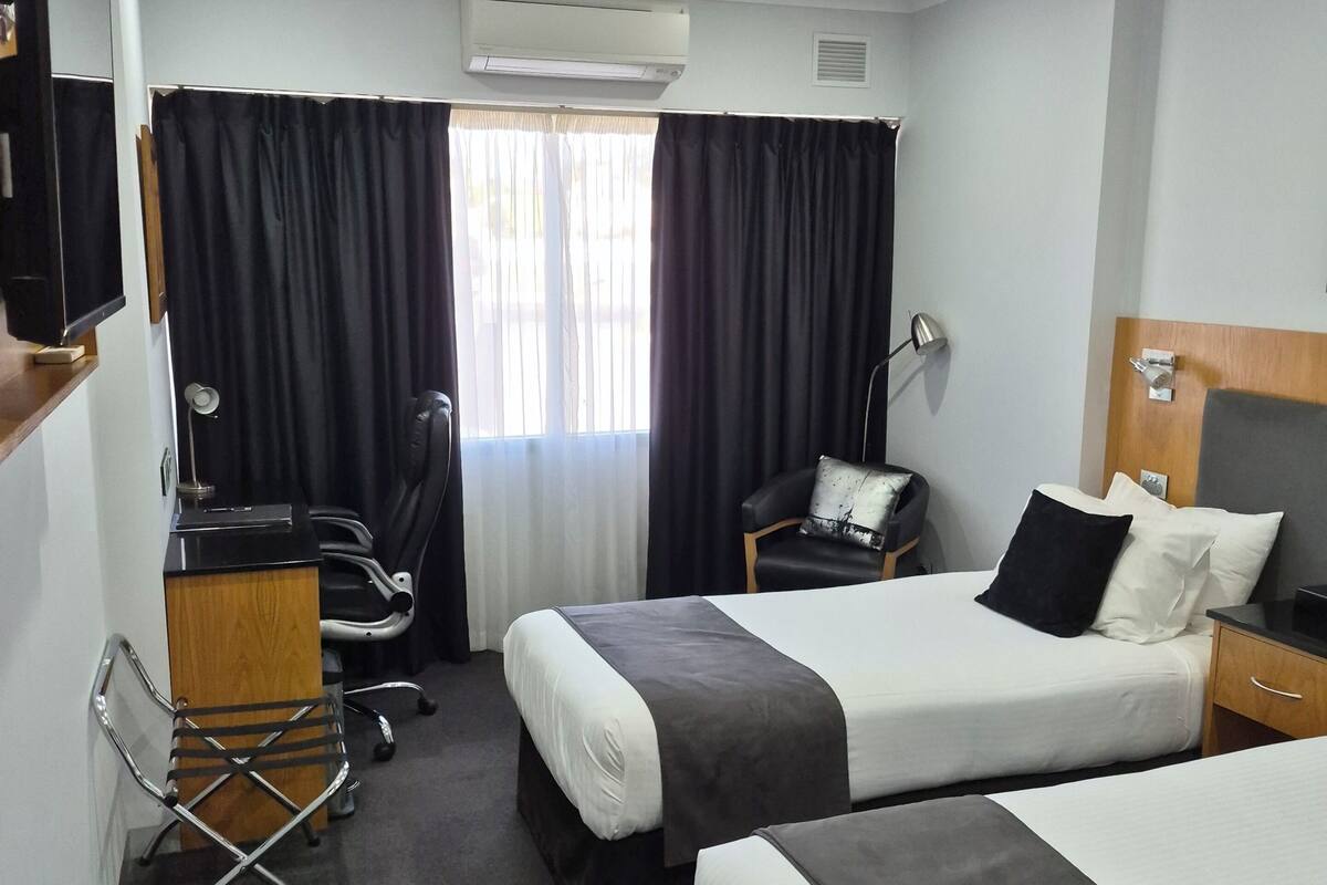 Habitación de hotel con dos camas, un escritorio, una silla, un televisor y un equipo de aire acondicionado.