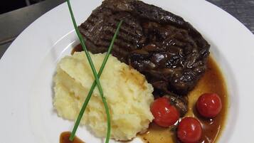 Um prato com bife, purê de batatas e tomates cereja.