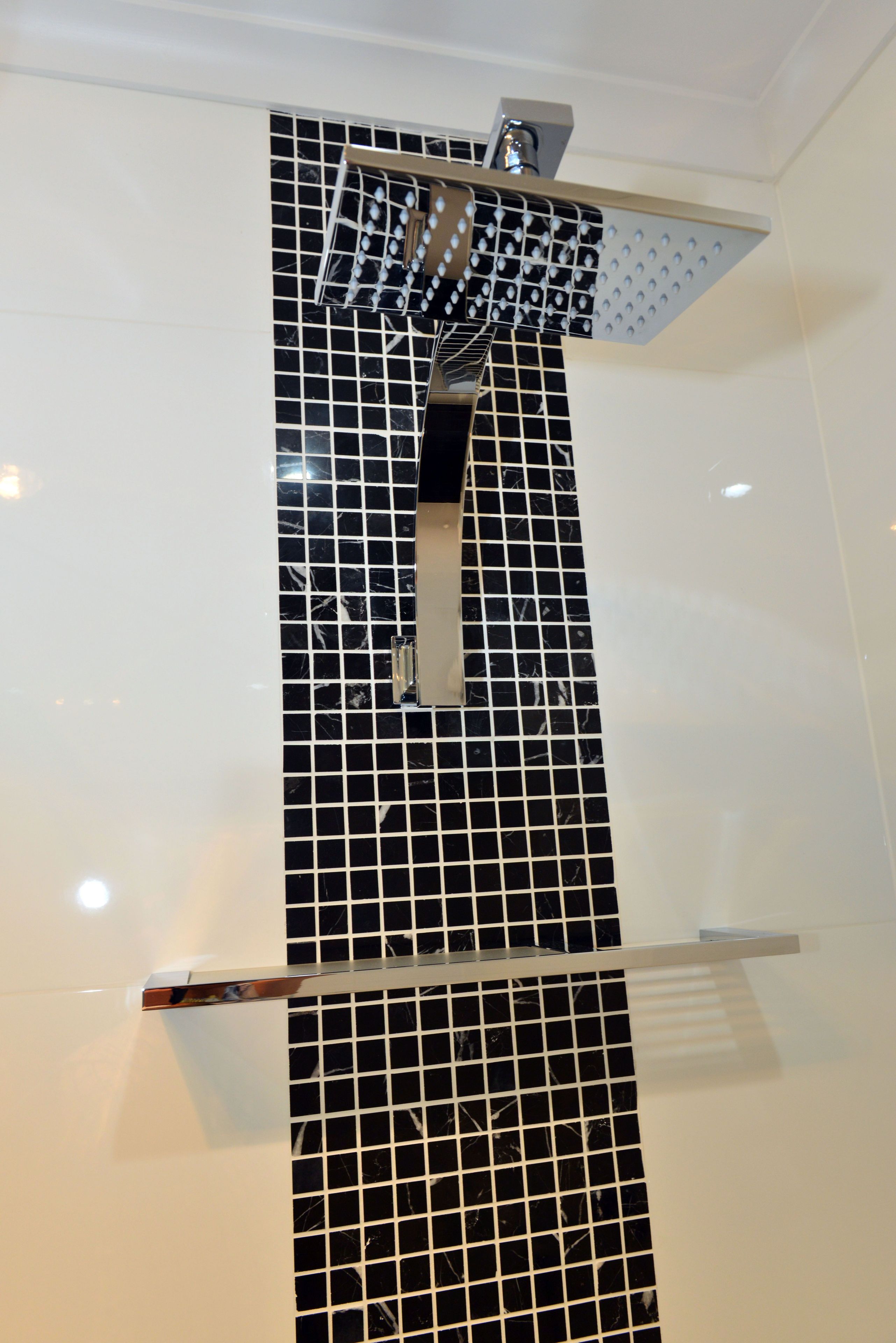 Un baño con pared de baldosas blanco y negro, ducha y pasamanos.