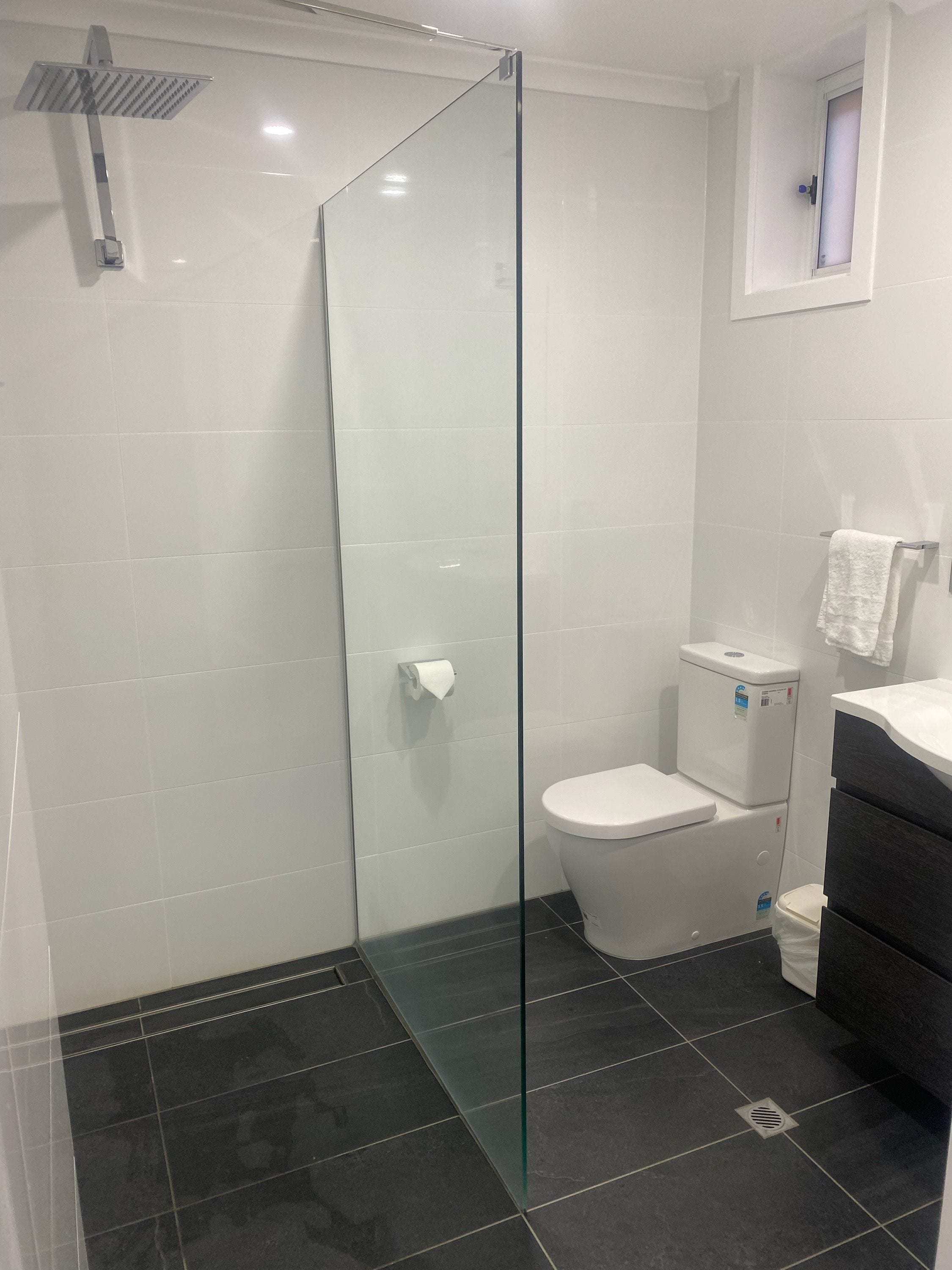 Un baño moderno con cabina de ducha de vidrio, un inodoro y un suelo de baldosas oscuras.