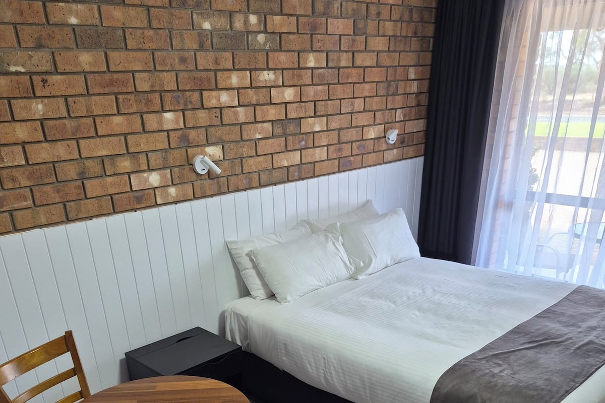 Habitación de hotel con pared de ladrillo, cama con ropa de cama blanca, una mesa de madera y una silla.