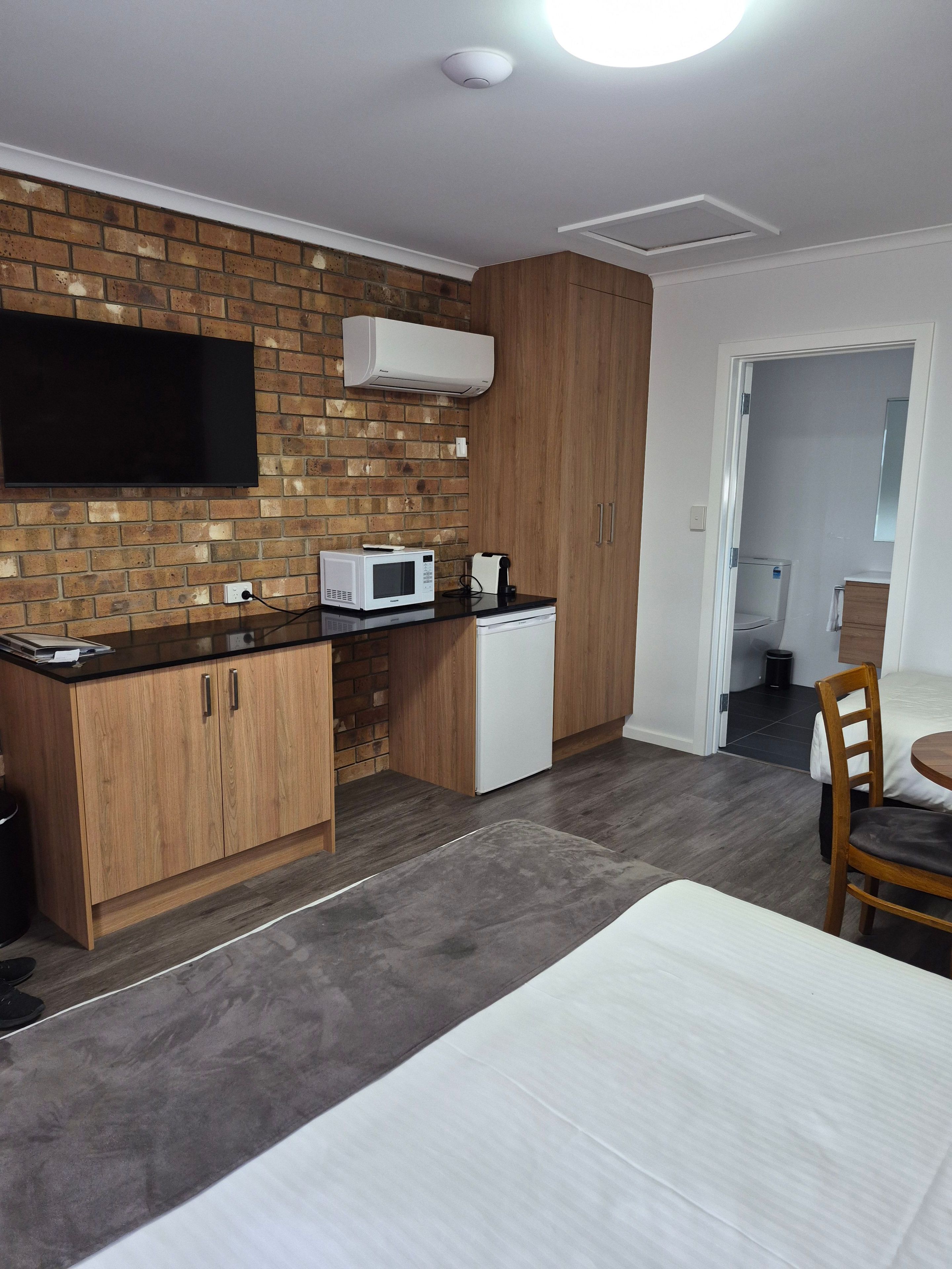 A compact kitchen with a microwave, a coffee maker, and a flat-screen TV mounted on a brick wall.