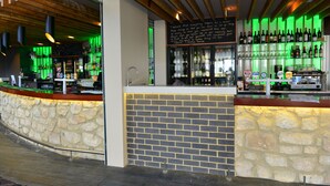 Un bar con mostrador de piedra, pared de ladrillo, estantes con botellas y una pizarra con escritura.