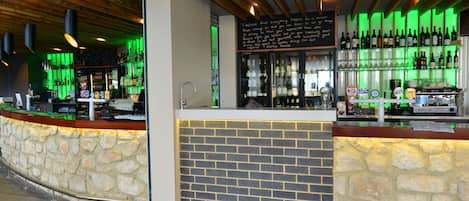 A bar with a stone counter and a brick wall, shelves with bottles, and a chalkboard with writing.