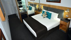 Una habitación de hotel con una cama grande, mesitas de noche, un espejo, un escritorio y un armario.