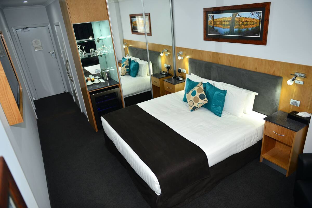 Una habitación de hotel con una cama grande, mesitas de noche, un espejo, un escritorio y un armario.