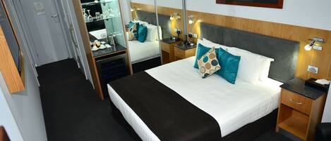Una habitación de hotel con una cama grande, mesitas de noche, un espejo, un escritorio y un armario.