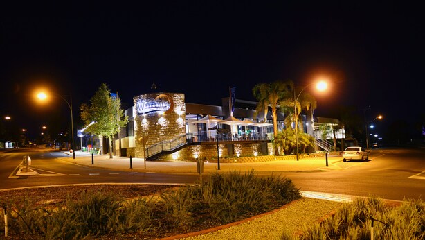 Un hotel bien iluminado con un letrero llamativo, una escalera que conduce a la entrada y un área de estacionamiento.
