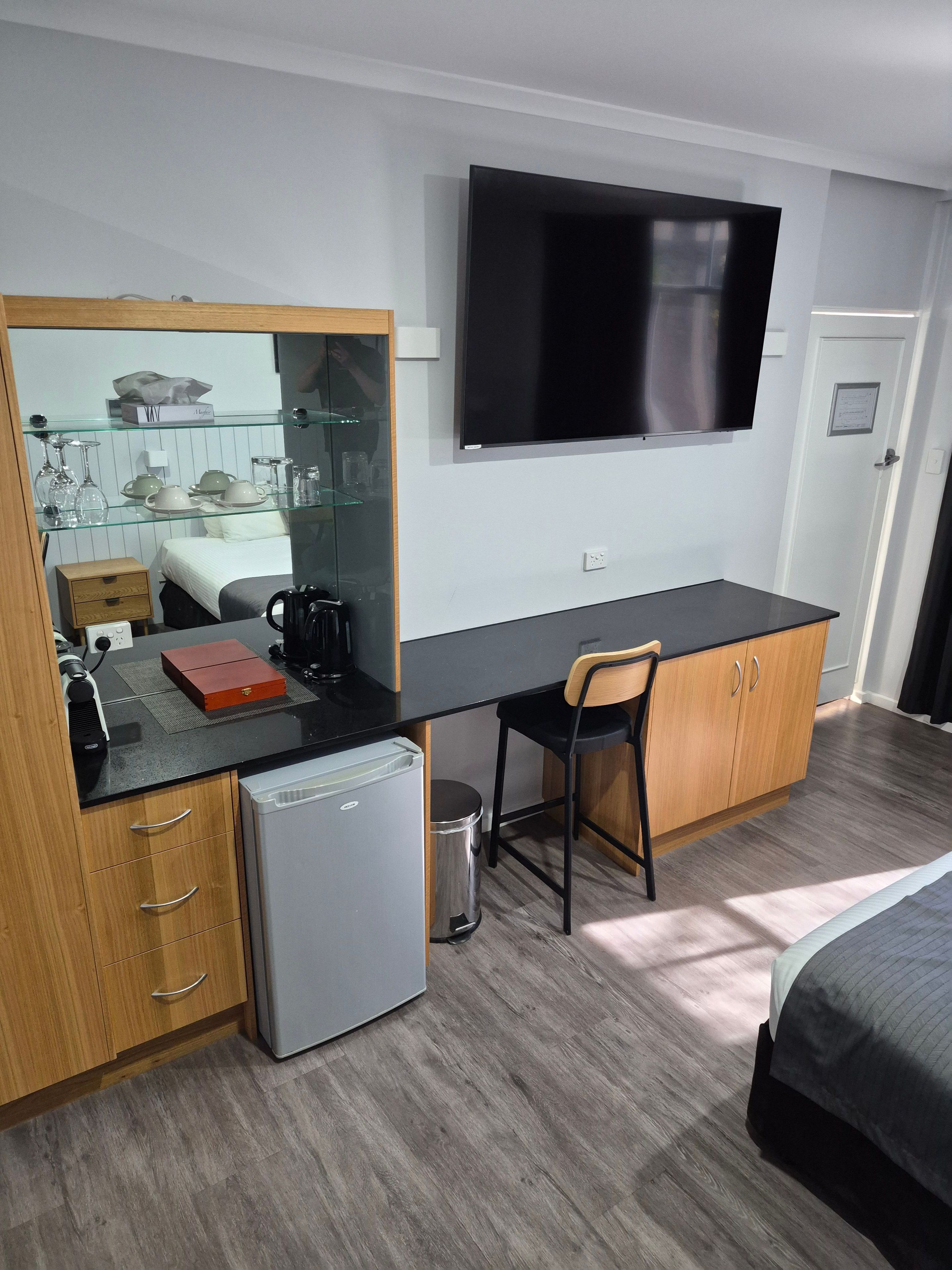 Une chambre d’hôtel compacte comprenant un coin cuisine, un lit, un bureau avec une chaise, une télévision et un petit réfrigérateur.
