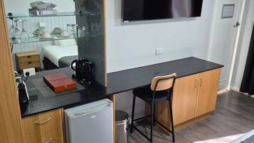 Une chambre d’hôtel compacte comprenant un coin cuisine, un lit, un bureau avec une chaise, une télévision et un petit réfrigérateur.