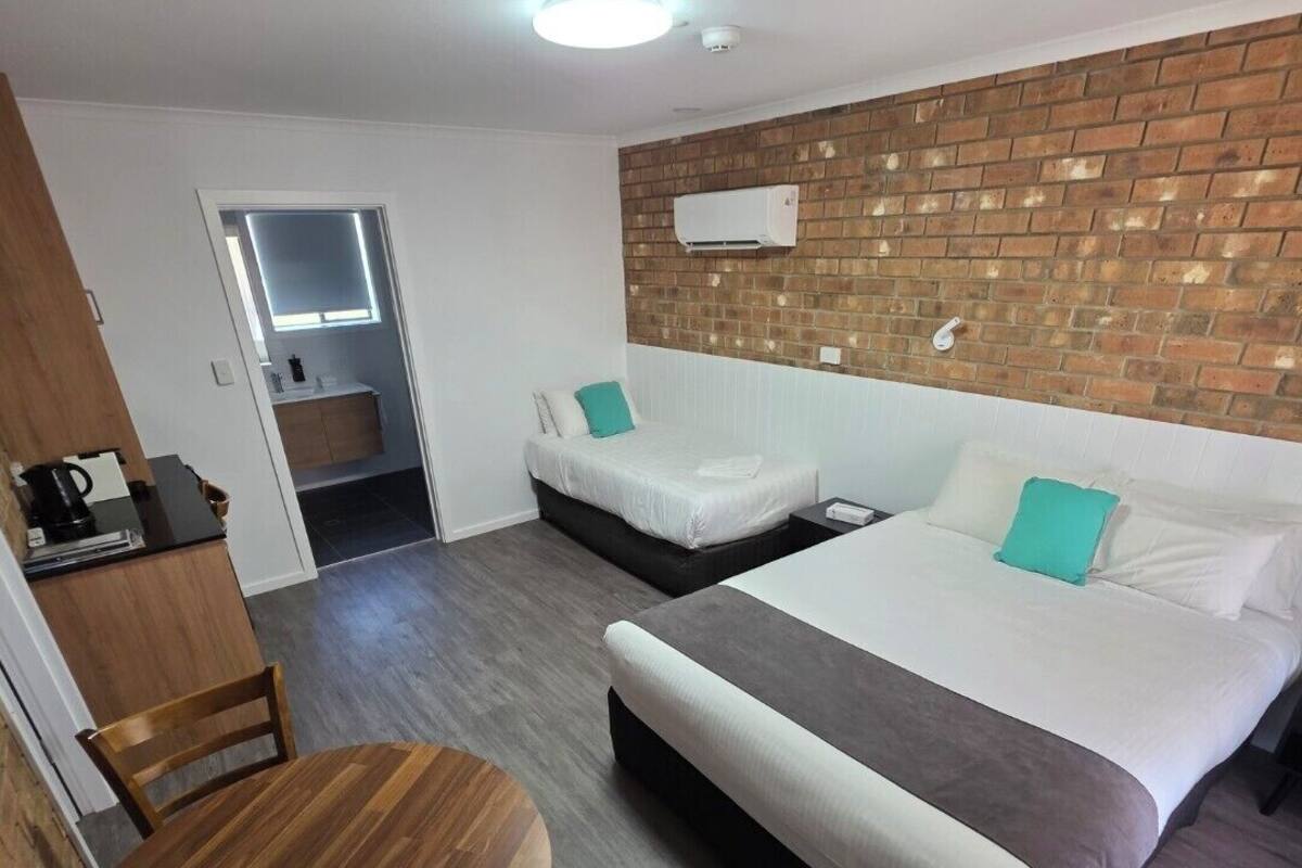 Habitación de hotel con una cama grande, otra más pequeña, un escritorio con silla y una mesa redonda de madera.