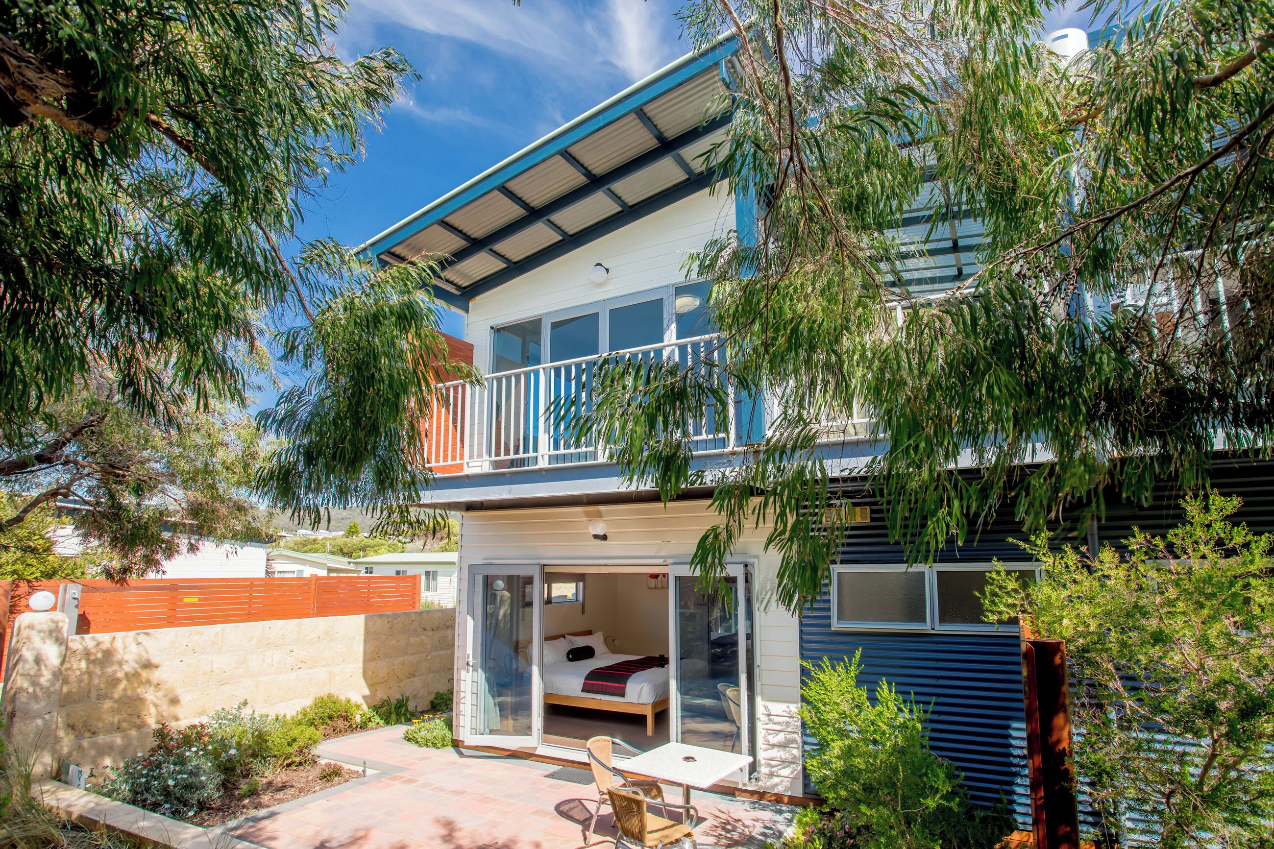 A two-story house with a balcony, a sliding glass door leading to a bedroom, and a small patio area.