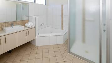 A modern bathroom with a large bathtub, a separate shower area, and a vanity with a sink and mirror.