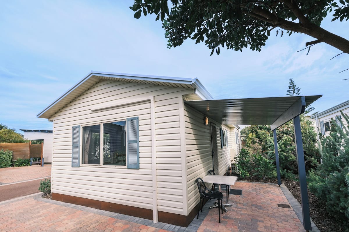 A single-story house with a covered patio area, a small table, and a chair.