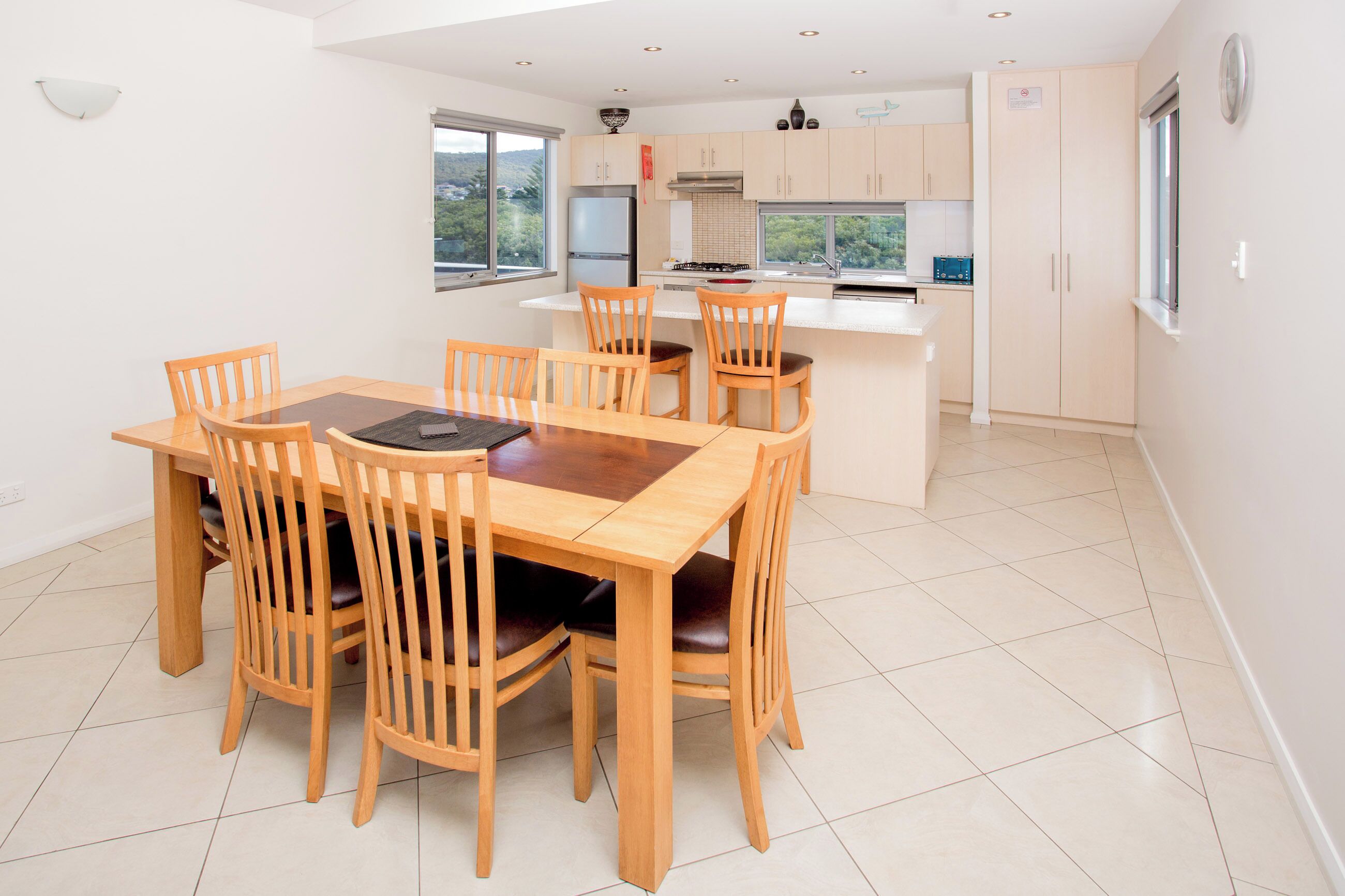 A modern kitchen with a dining area, featuring a wooden table and chairs, a built-in oven, and a view of the outdoors.