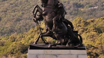 A statue of a figure on horseback, set on a stone pedestal, overlooking a coastal landscape with hills and a lighthouse in the distance.
