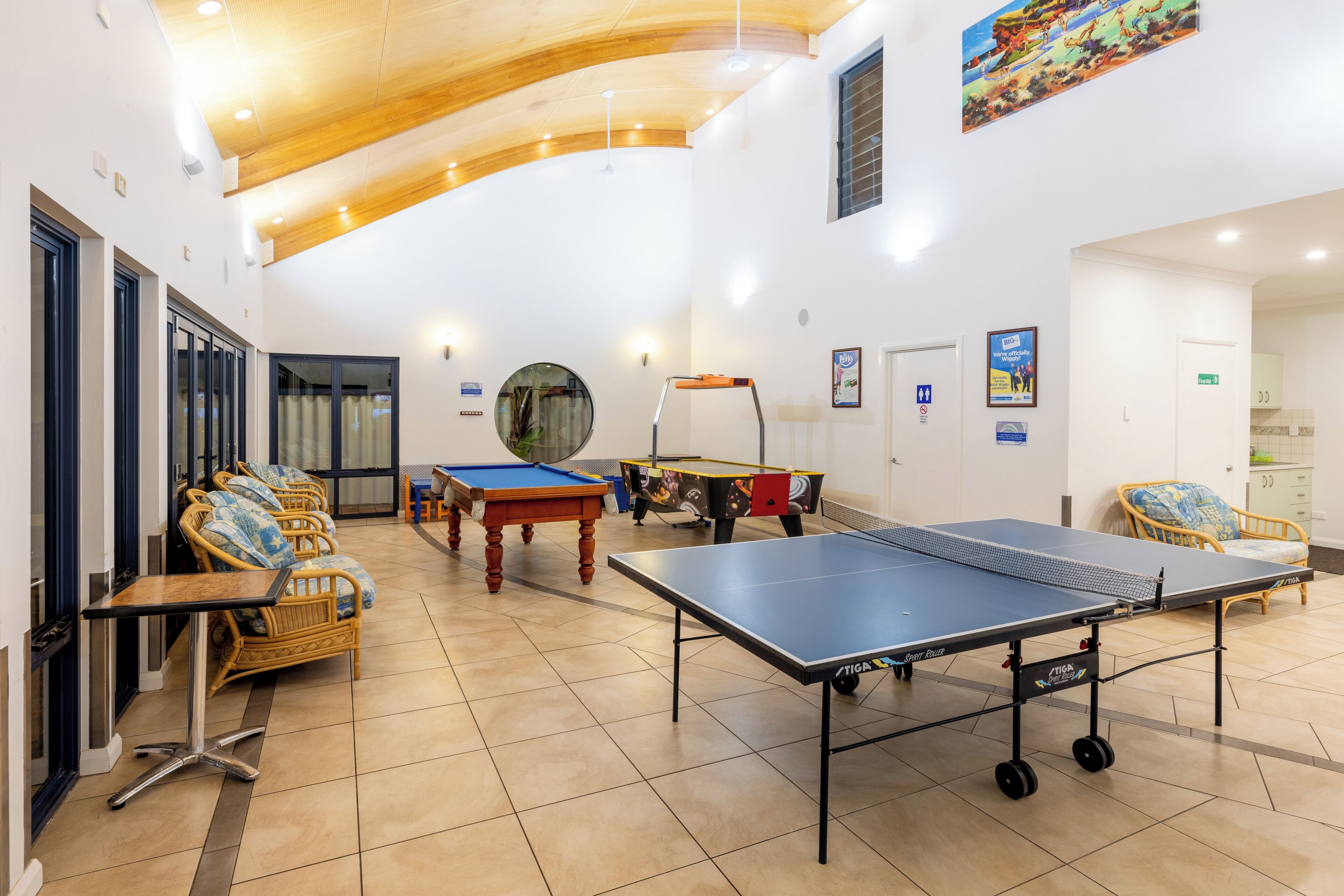 A spacious indoor area with a ping pong table, pool table, and seating area with wicker chairs.