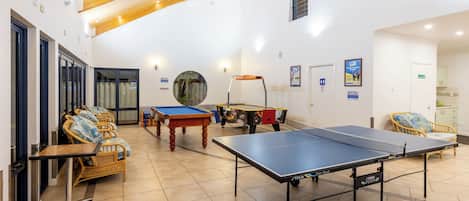 A spacious indoor area with a ping pong table, pool table, and seating area with wicker chairs.