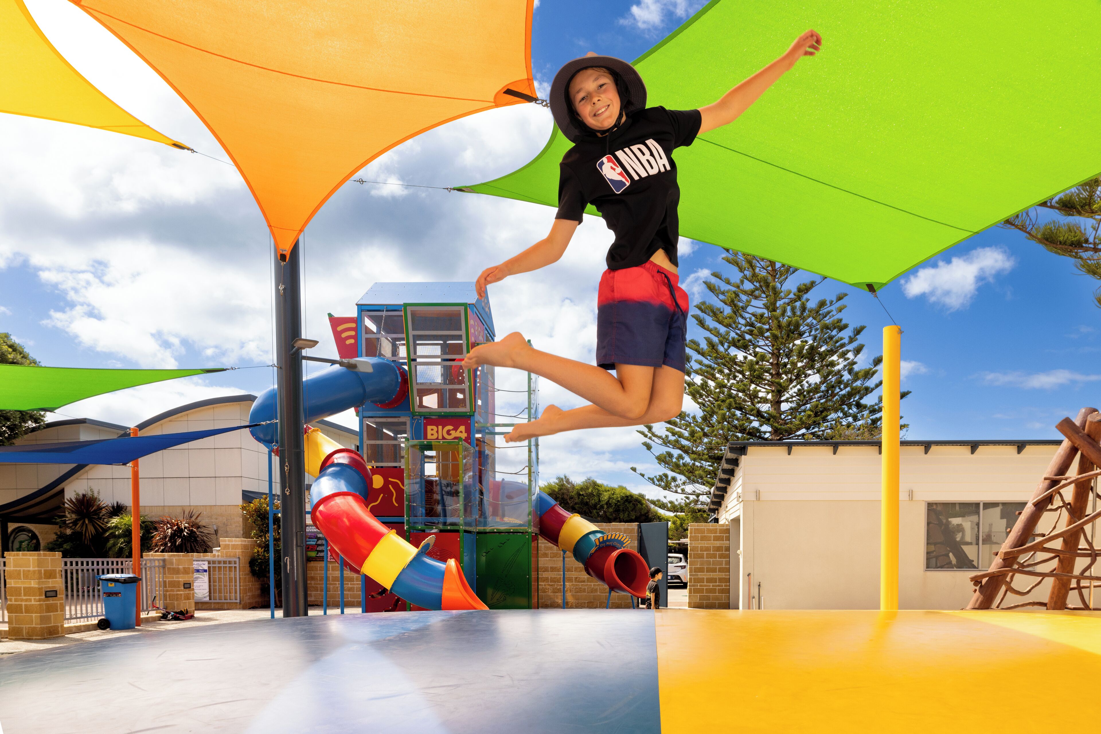 A playground with slides and climbing structures, surrounded by a fenced area and a building in the background.
