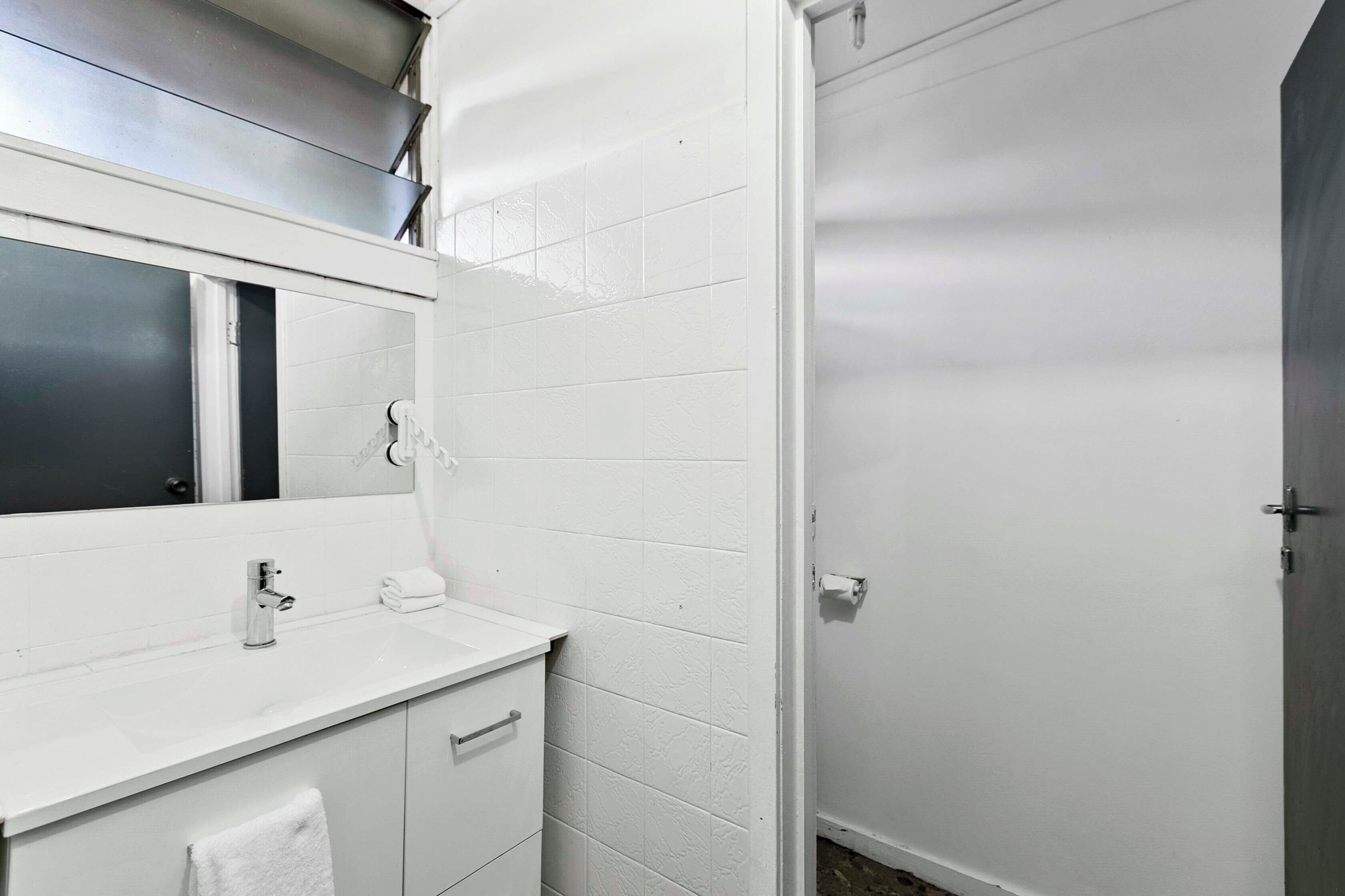 Un baño con azulejos blancos, un lavamanos, un espejo y una puerta.