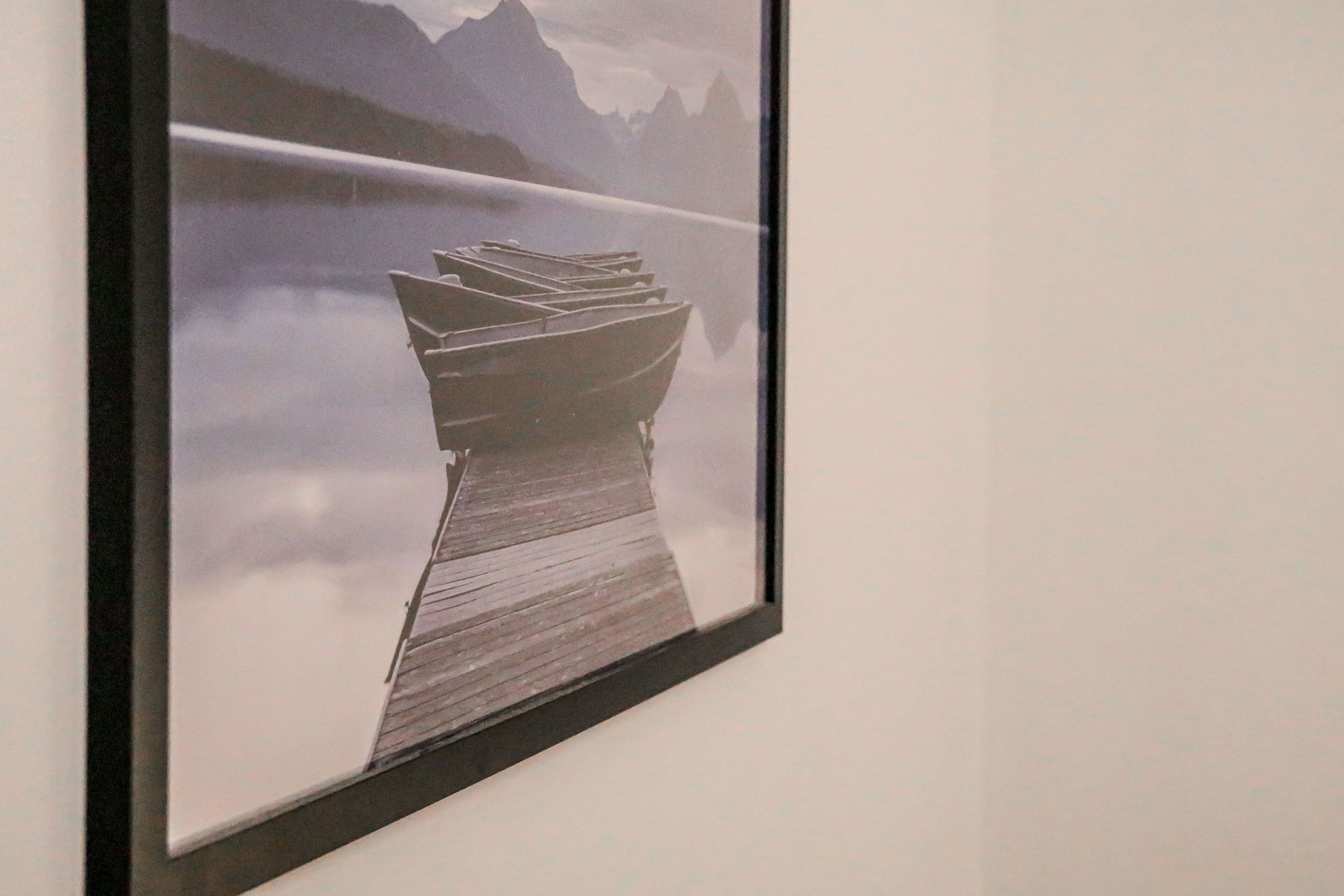A framed artwork of a wooden dock extending into a misty lake with mountains in the background.